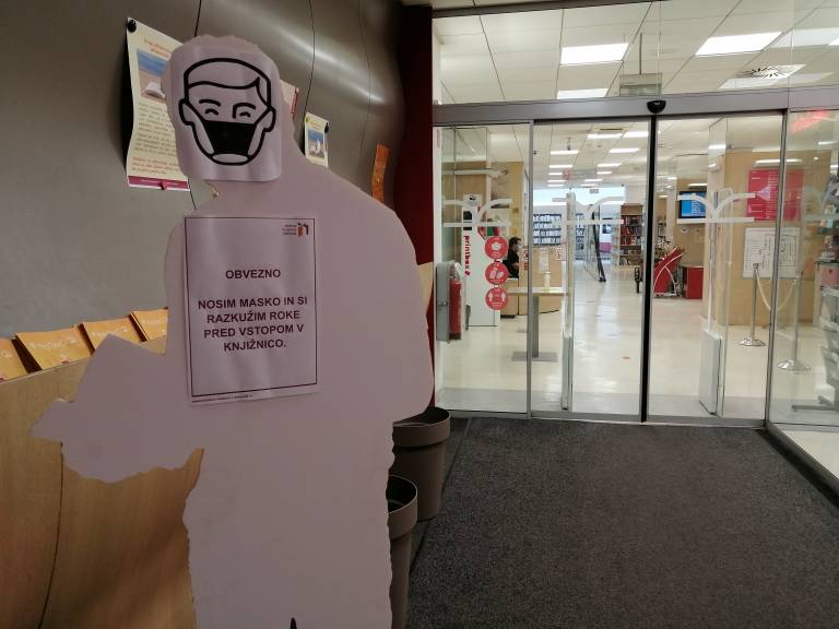 Obvestilo ob vstopu v knjižnico o obvezni nošnji maske in razkužitvi rok. 